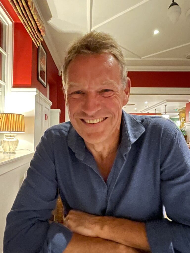 A picture of Paul Stewart smiling to camera in a blue shirt.