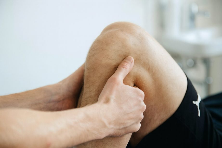 An image of a person's knee being held and manipulated by two hands of another person in the manner of a physiotherapist.
